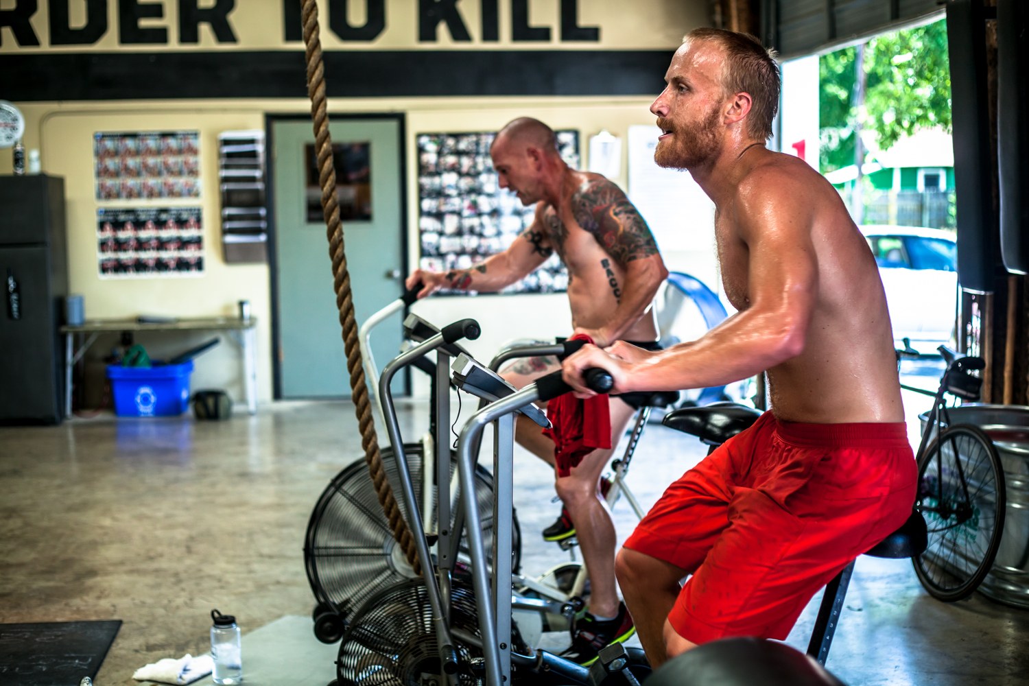 Athletes grinding hard on assault bikes in a tough gym, building rounds-deep conditioning
